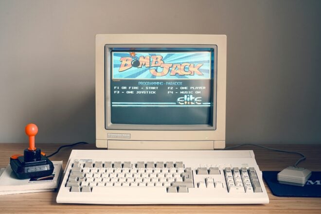 A retro computer with an old keyboard and a joystick, with an old game on the screen.
